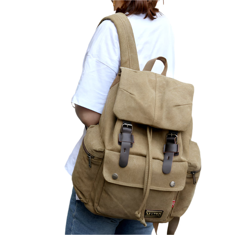 A person wearing a beige canvas backpack with multiple compartments and leather buckles.